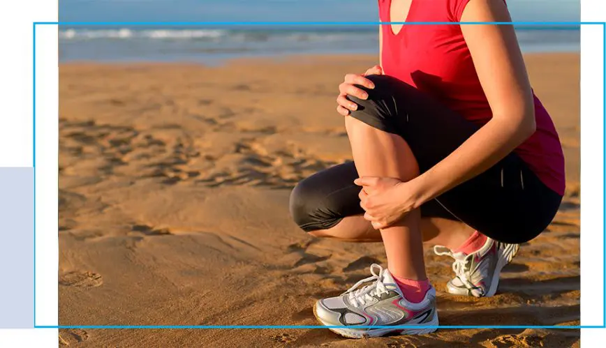 A woman kneeling down on the beach with her legs crossed.